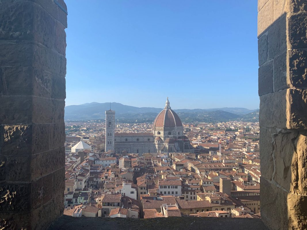 Looking out from the top of the Palazzo Vecchio over the red rooftops of Florence with Florence Cathedral and the Duomo in the skyline and the tuscan mountains in the distance