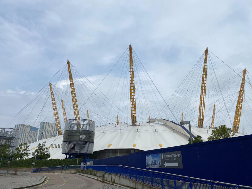 View of the outside of the O2 dome, a white tent like structure with 12 yellow poles sticking out of the top