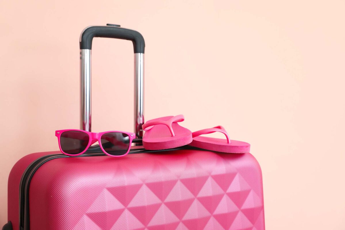 Image of a pink suitcase with a pair of pink sun glasses and flip flops sitting top.