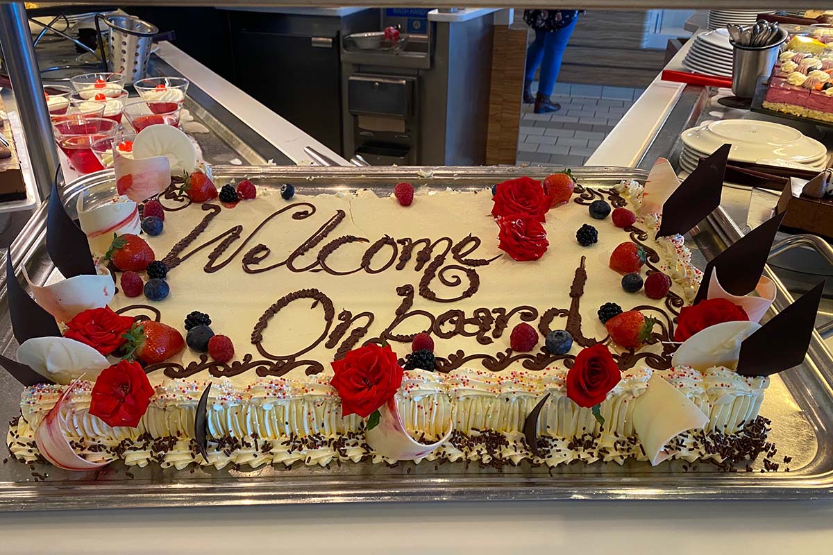 A cake decorated with icing saying Welcome on board on display in a cruise ship's buffet