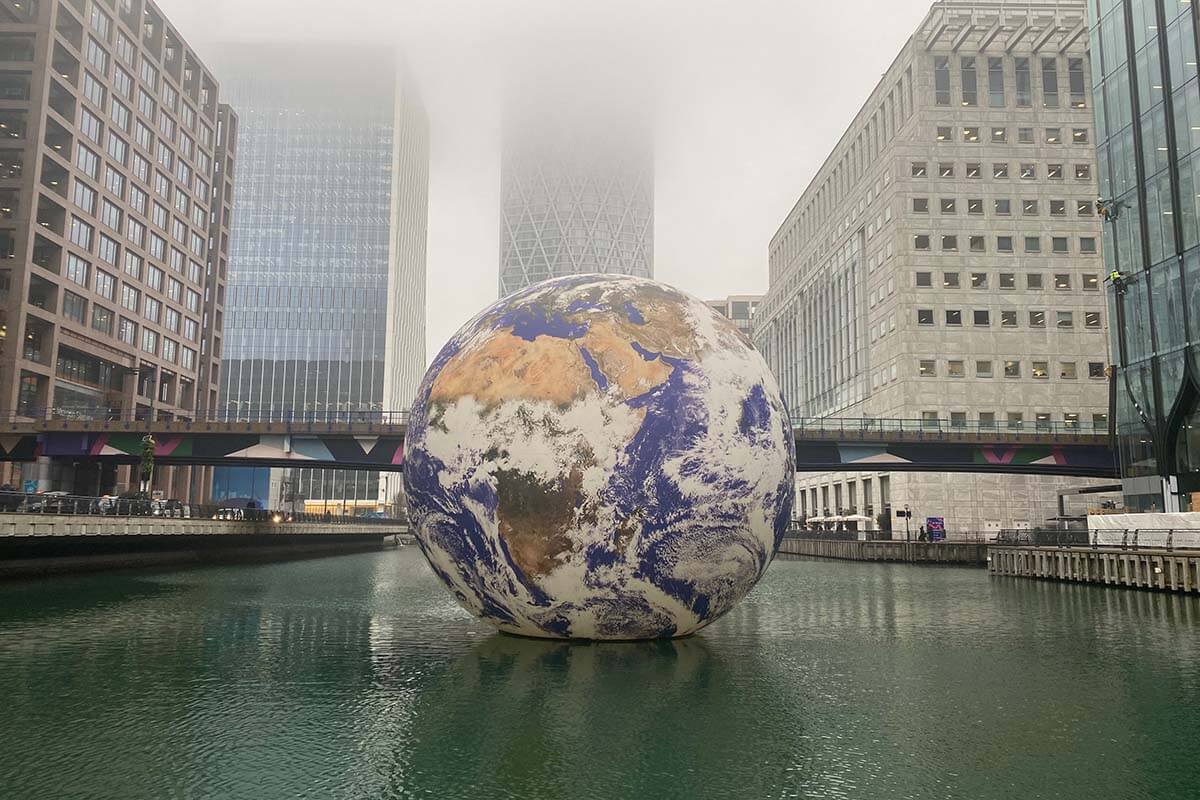 image of a globe floating a dock with railway line in the background crossing the water and skyscraper in the distance.