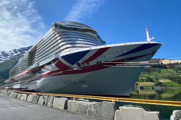image of the front of cruise ship docked in a fjord in Norway with a blue skies behind, green landscape and blue fjord water.