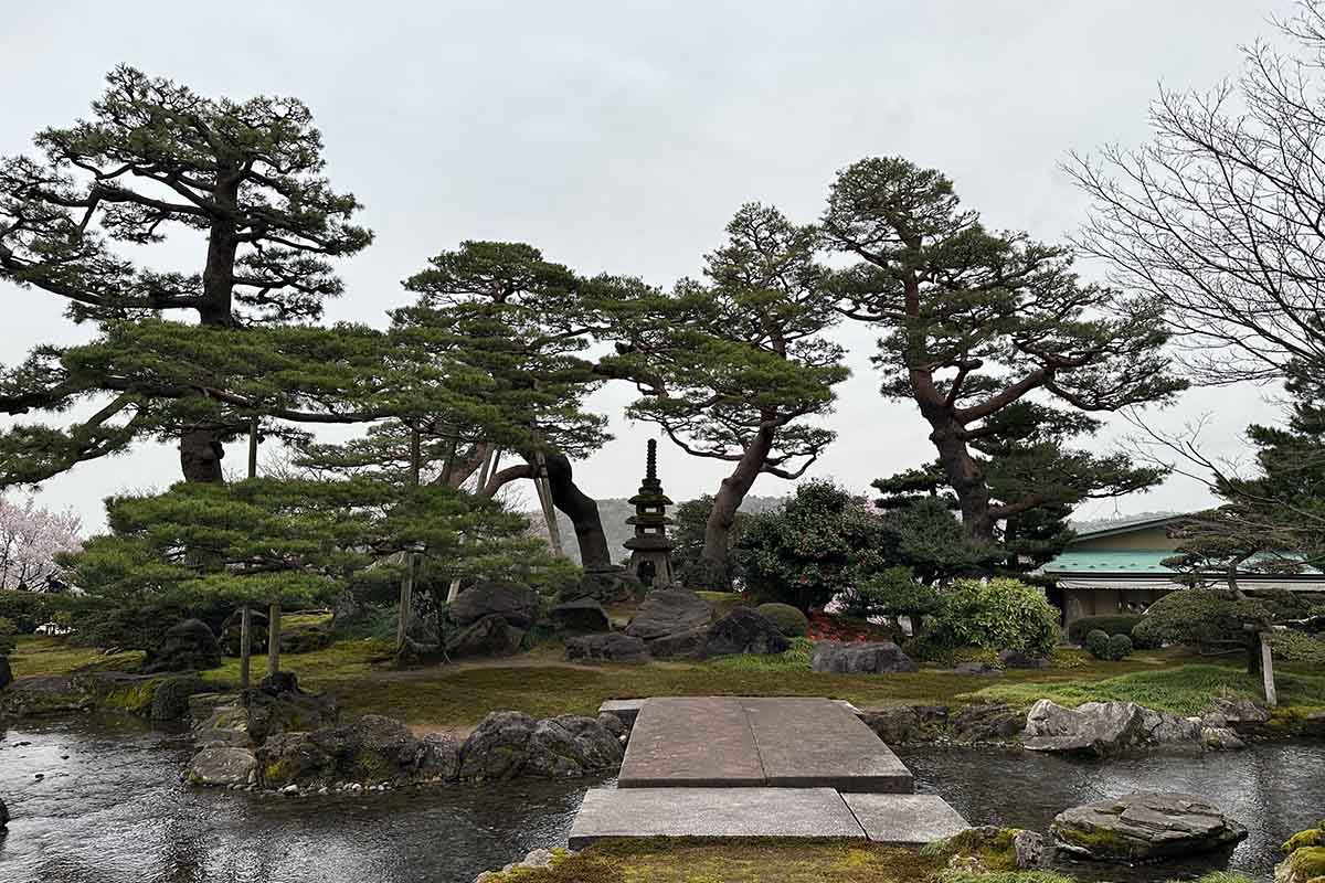 image of a Japanese garden in Kenrokuen Gardens with a pond, stones and trees.