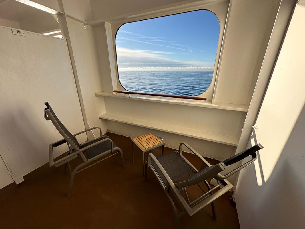 image of a sheltered balcony on Cunard's Queen Mary 2. The large balcony has two chairs, a small table and a view of the sea and sky cut out from the ships hull