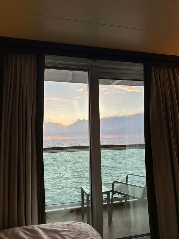 A view out to sea from the bed in solo balcony cabin on Britannia. A chair and table are on the balcony with the sea stretching into the distance.