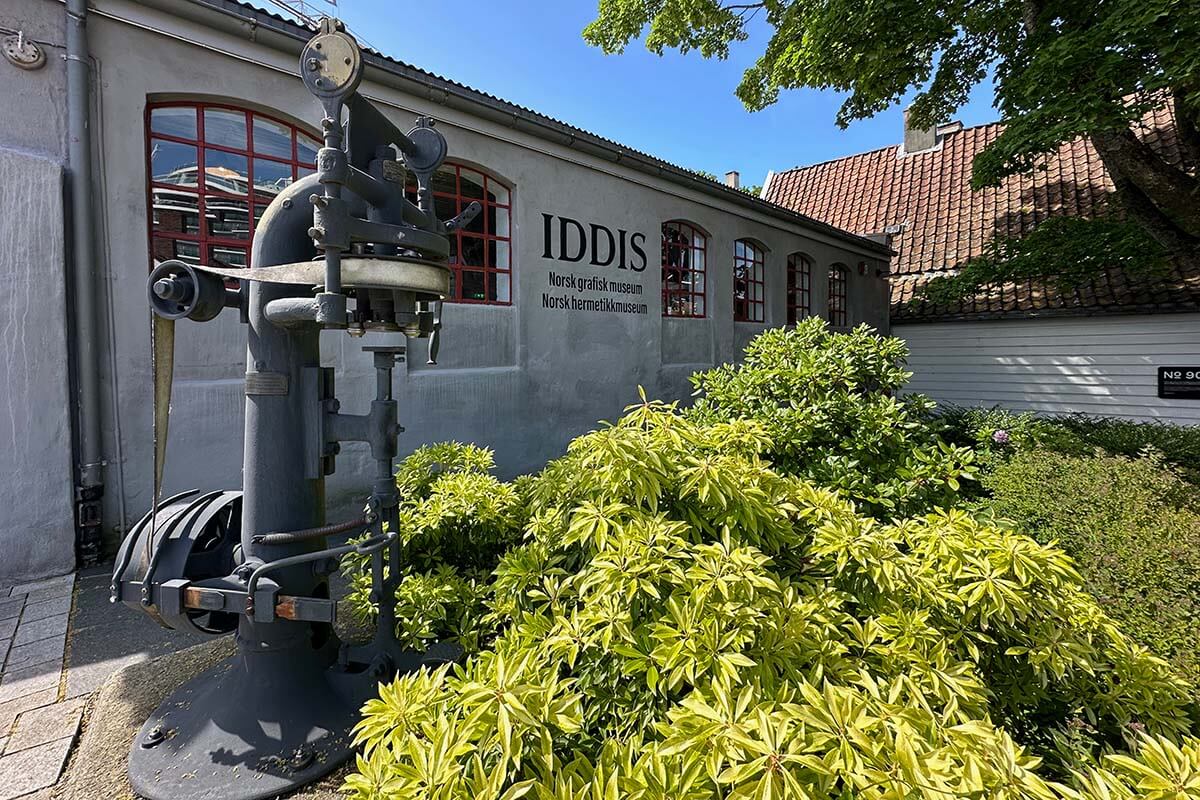 The outside of the Norwegian Canning museum building with a piece of equipment and .green plants in front.