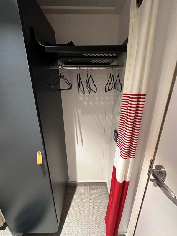 Hanging space with a red and white curtain in a solo insider cabin on Virgin Voyages.