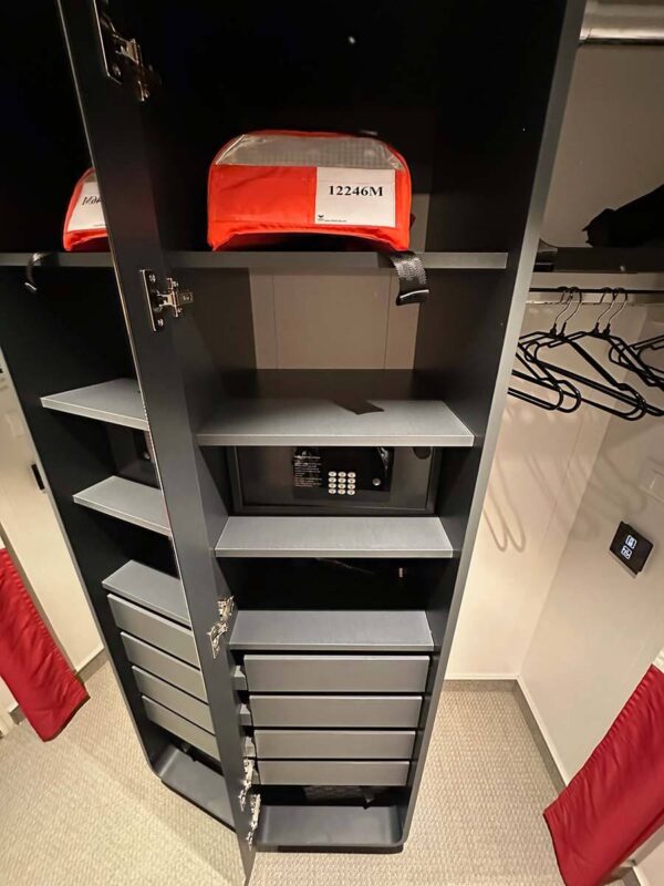 image of a cupboard with an open door revealing three drawers and four shelves. A safe and life jacket sit on the shelves. 