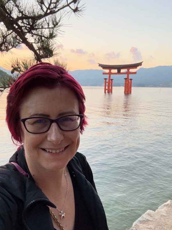 Emma smiling at sunset with Japan’s famous floating torii gate in the background, capturing a peaceful moment by the water.