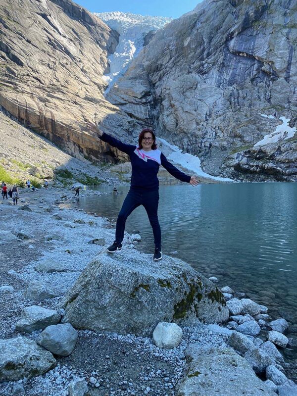 Emma standing on a rock in front of a glacier and alpine lake, surrounded by rugged mountain scenery.