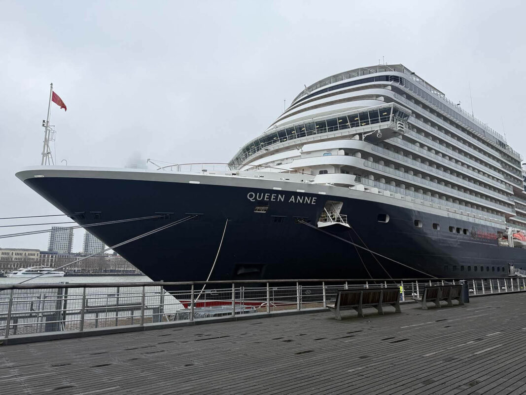 Cunard’s Queen Anne docked in Rotterdam with its navy hull, white balconies, and prominent bow with the ship’s name in bold white letters.