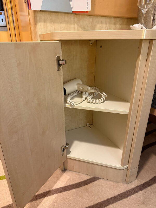 Open cabinet in an inside cabin on Ambassador Ambition showing a built in hairdryer with a coiled cord stored on the shelf.