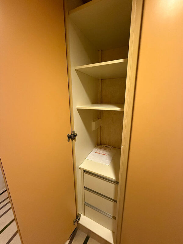 Open wardrobe in an inside cabin on Ambassador Ambition with shelves and drawers for storage.