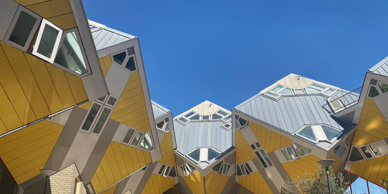 Looking up at the famous yellow Cube Houses in Rotterdam Netherlands with their unusual tilted cube shapes and angular windows. The geometric buildings stand against a clear blue sky.